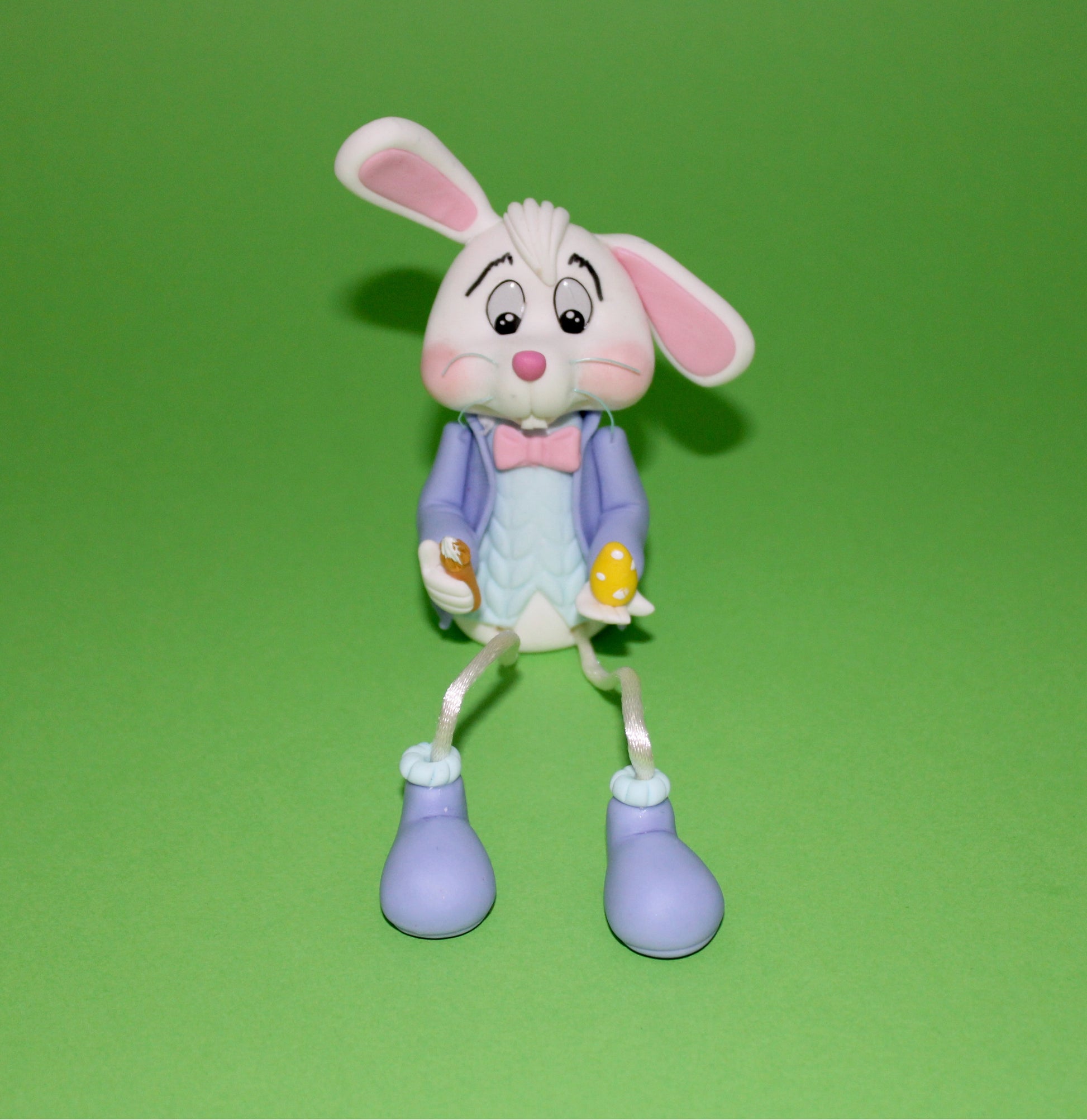figurine lapin de Pâques décorative assis jambes pendantes et pieds suspendus en train de peindre un oeuf de Pâques, cadeau de pâque pour garçon 